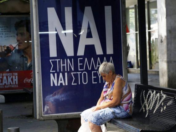 A woman waits at a bus stop net to a poster reading “Yes to Greece yes to Euro” referring to the Sunday referendum in Athens on Saturday