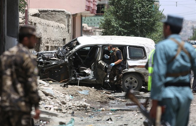 Afghan security personnel inspect a damaged vehicle at the site of a suicide attack that targeted a NATO convoy in Kabul Afghanistan Tuesday