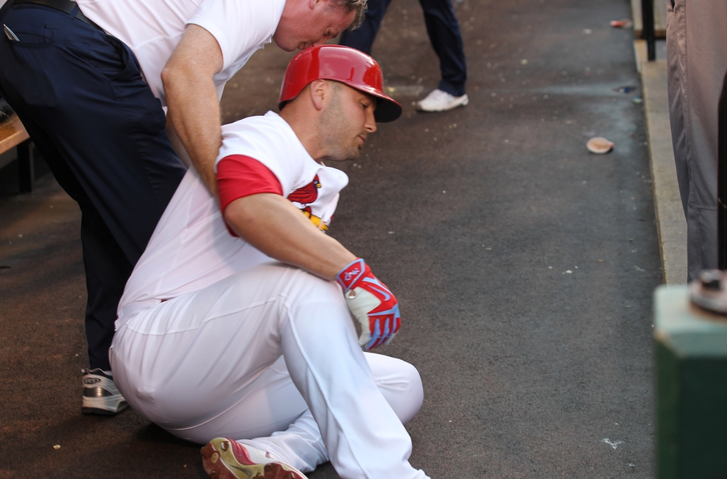 St. Louis Cardinals Matt Holliday is attended to by trainer Chris Conroy as he sits on the floor of the dugout after injuring his leg in the first inning against the Cincinnati Reds at Busch Stadium in St. Louis