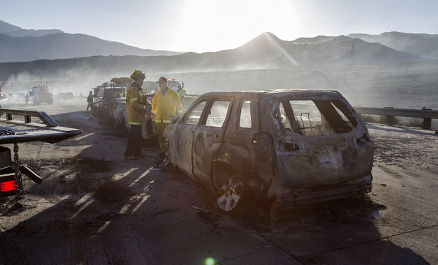 Firefighters work at the scene near burned cars on the 15 Freeway