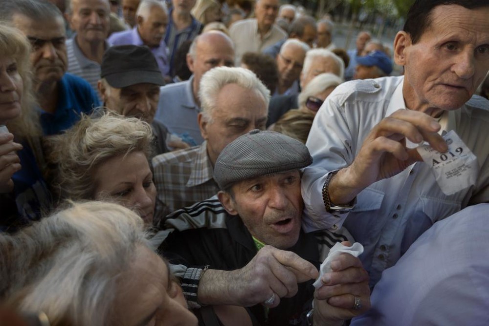 Pensioners holding their queue numbers try to enter a bank in Athens on Wednesday. About 1,000 bank branches across Greece were ordered by the government to reopen Wednesday to help desperate pensioners without ATM cards cash up to 120 euros from