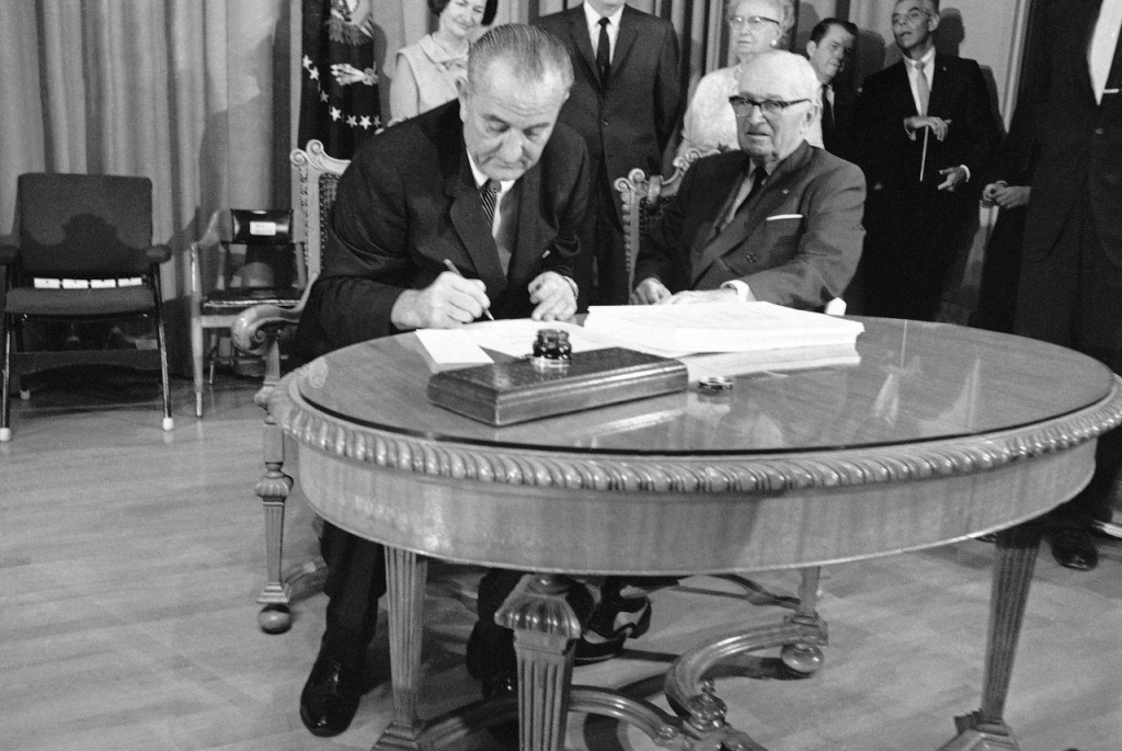 President Lyndon B. Johnson uses the last of many pens to complete the signing of the Medicare Bill into law at ceremonies at the Truman Library in Independence Missouri