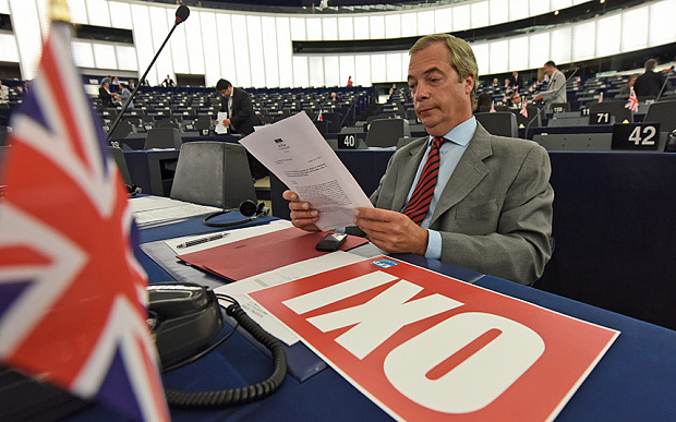 Nigel Farage has an'Oxi  placard on his desk as he reads in papers during the plenary session with