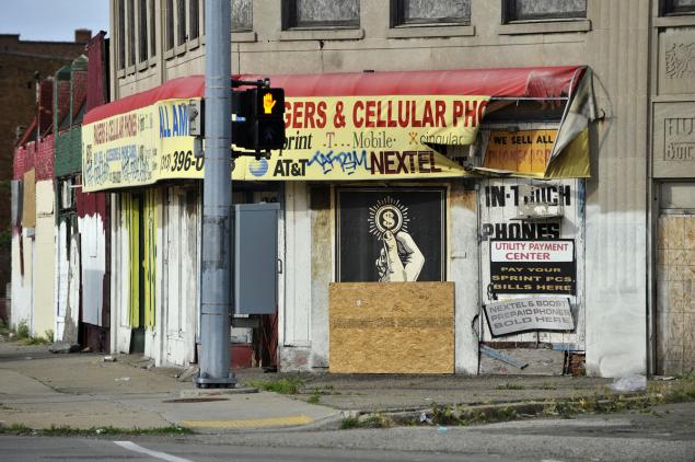 Anti-consumerism street art by Shepard Fairey is displayed on the side of a vacant building on Gratiot Avenue in Detroit. It has been partially covered by plywood