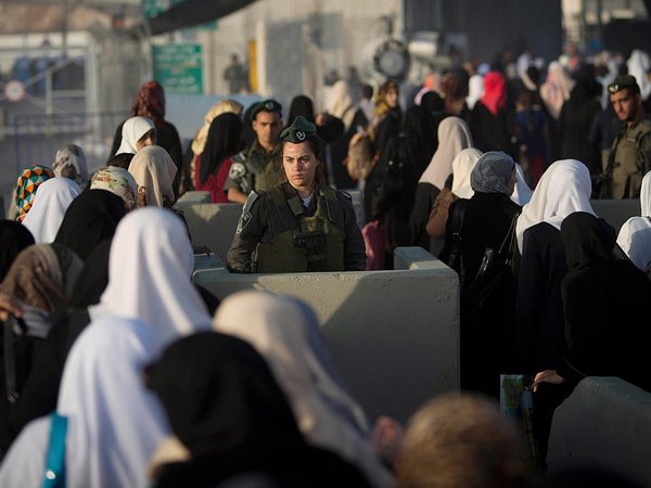 Palestinian women walk past an Israeli border police officer on their way to pray at the Al Aqsa Mosque in Jerusalem on the first Friday of the Muslim holy month of Ramadan at the Qalandia checkpoint between the West Bank city of Ramallah and Jerusalem