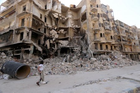 A man walks with the aid of a crutch past damaged buildings in the old city of Aleppo