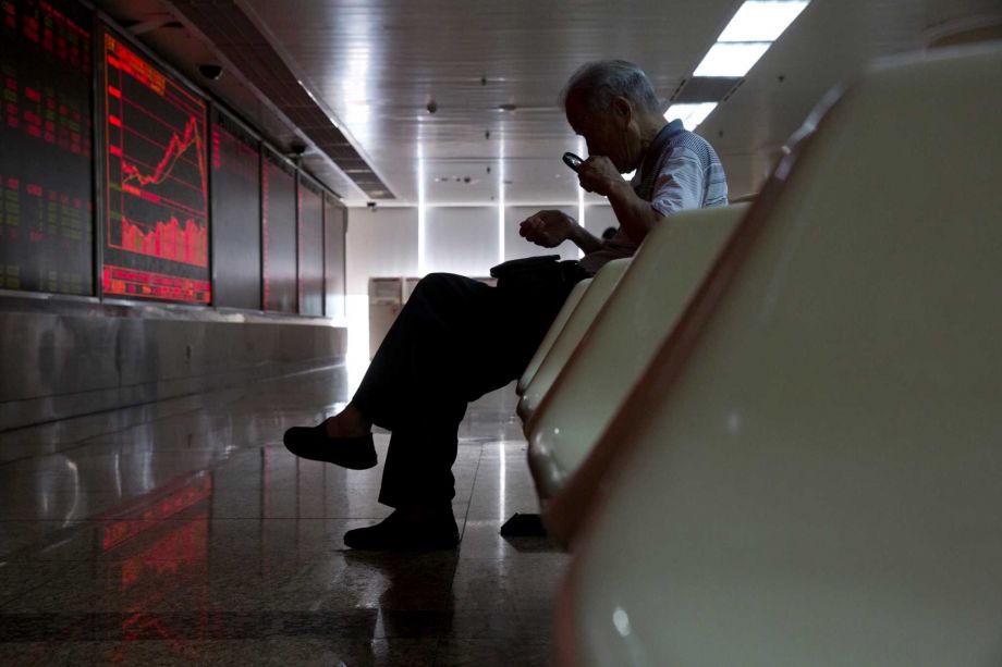 A Chinese stock investor uses a magnifying glass to look at his mobile phone screen as he monitors stock prices at a brokerage in Beijing China Thursday