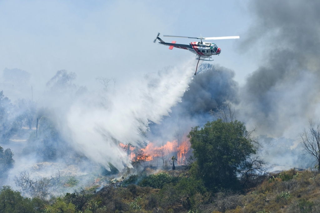 A helicopter drops water on a burning structure at Irvine Lake during the firefighting efforts on Monday in Orange County California. County fire officials say the blaze broke out Thursday in the unincorporated Silverado Canyon area near Irvine Lake. (Sa