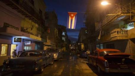 A tricycle taxi with a U.S. flag is parked on a street in Havana