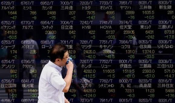 A man walks past a display showing stock prices in Tokyo