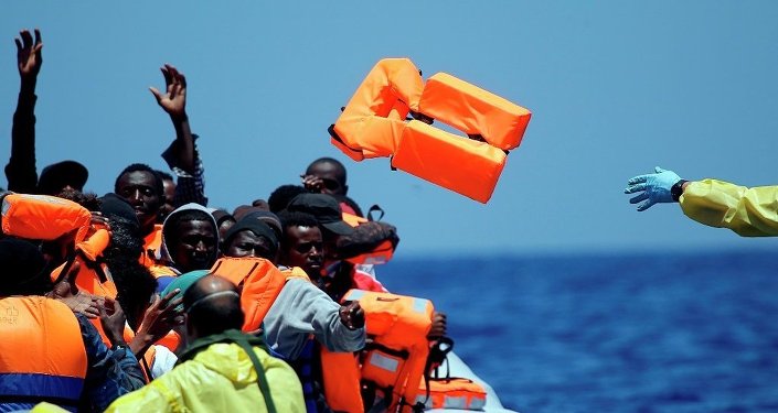 A Belgian nav.y sailor passes life vests to migrants sitting in a rubber boat as they approach the Belgian Navy Vessel Godetia during a search and rescue mission in the Mediterranean Eea off the Libyan coasts Tuesday