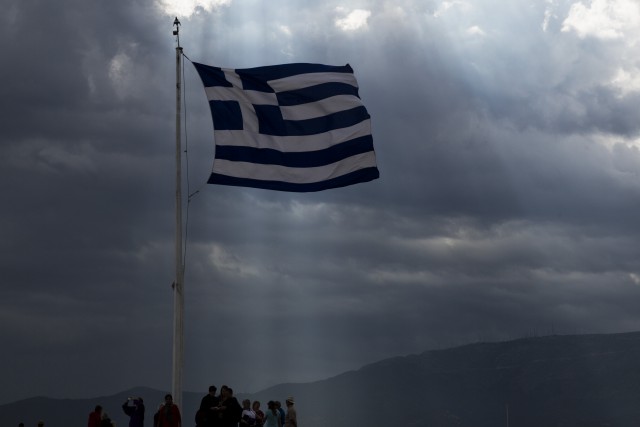 A Greek flag waves as the sun's rays shine through clouds at the ancient Acropolis hill in Athens Monday