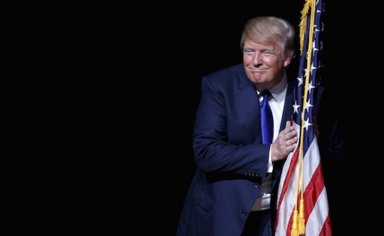 Republican presidential candidate Donald Trump hugs a U.S. flag as he takes the stage for a campaign town hall meeting in Derry N.H. on Aug. 19