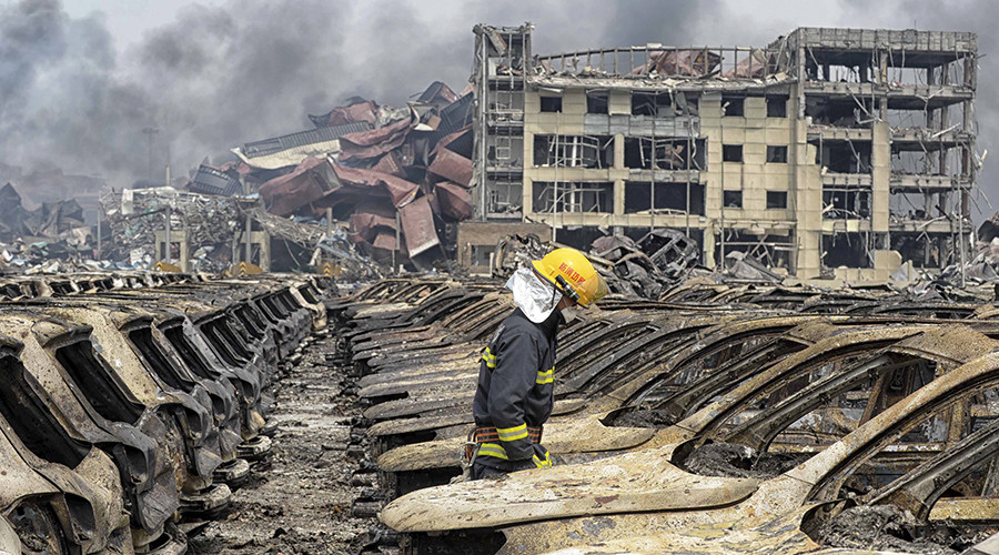 A firefighter walks among damaged vehicles as smoke rises amidst shipping containers at the site of Wednesday night's explosions at Binhai new district in Tianjin China