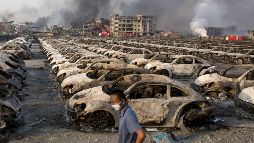 A man walks past the charred remains of new cars at a parking lot near the site of an explosion at a warehouse in northeastern China's Tianjin municipality Aug. 13 2015