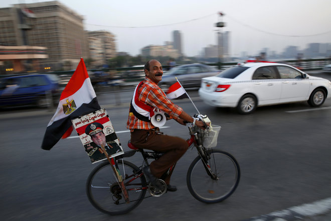 A supporter of Egyptian President Abdel Fattah el-Sissi carries his poster on his bike as he celebrates with others for Thursday's opening of the new extension of the Suez Canal riding on the Qasr El Nile Bridge in Cairo Egypt Wednesday Aug. 5 2015