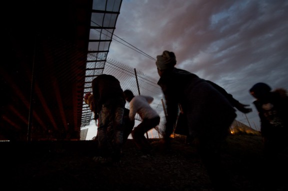 Migrants cross through a hole in the fence as they attempt to access the Channel Tunnel in Calais on Monday