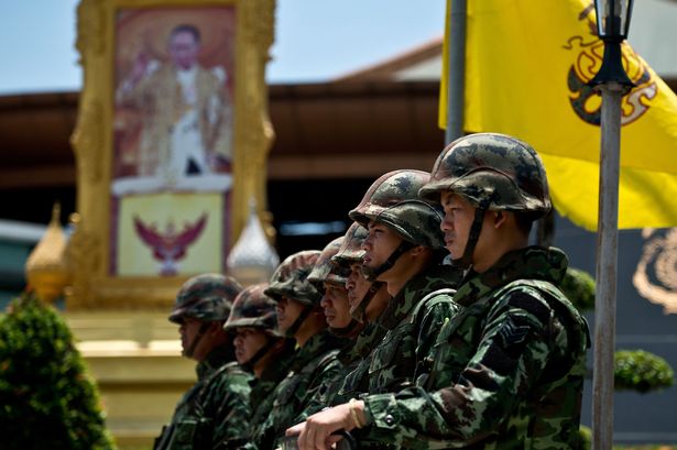 A portrait of Thai King Bhumibol Adulyadej is seen as Thai Army soldiers stand guard