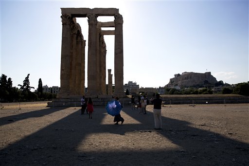 A woman carries a parasol for the strong afternoon sun as a group of tourists walk around the ruined ancient Temple of Olympian Zeus with the Acropolis hill in the background in central Athens on Wednesday Aug. 19 2015. Germany's parliament overwhelmi