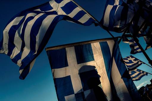 A pro Euro demonstrator is silhouetted behind a Greek flag during a rally outside the Greek Parliament in Athens in this