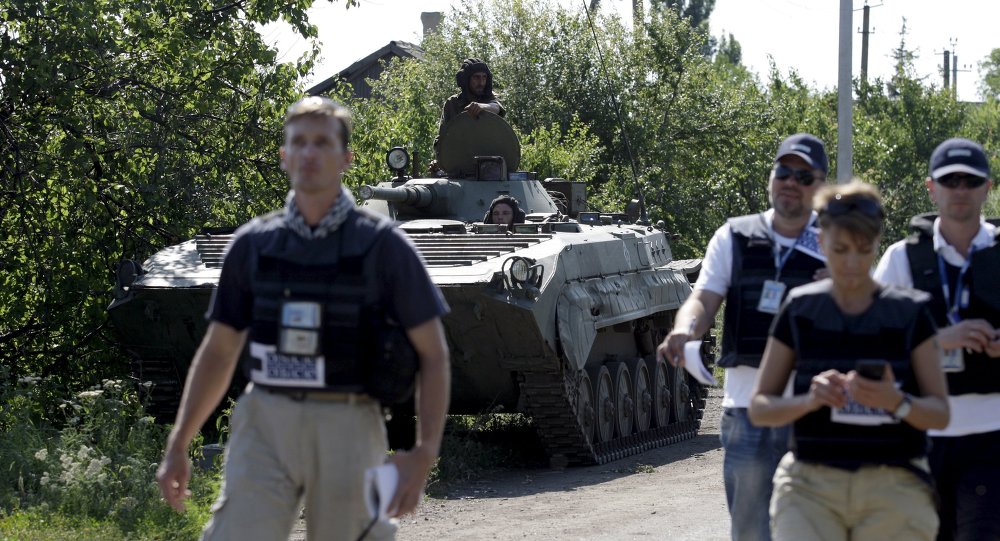 Members of the Organisation for Security and Co-operation in Europe walk past an armoured personnel carrier of the self-proclaimed Donetsk People's Republic forces outside the village of Novolaspa in Donetsk region Ukraine