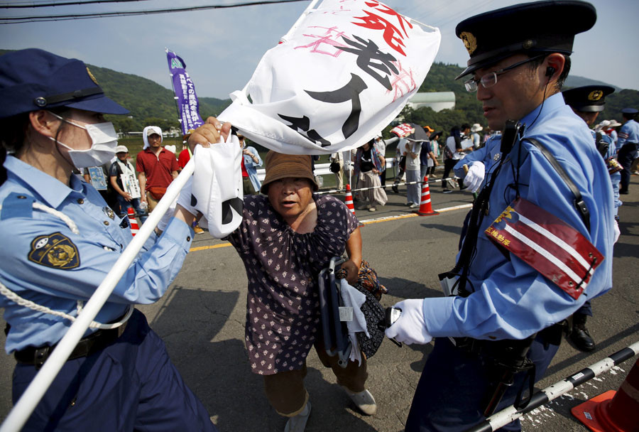 A protester is stopped by police officers during a march against the restarting of the plant in front of an entrance of Kyushu Electric Power's Sendai nuclear power station in Satsumasendai Kagoshima prefecture Japan