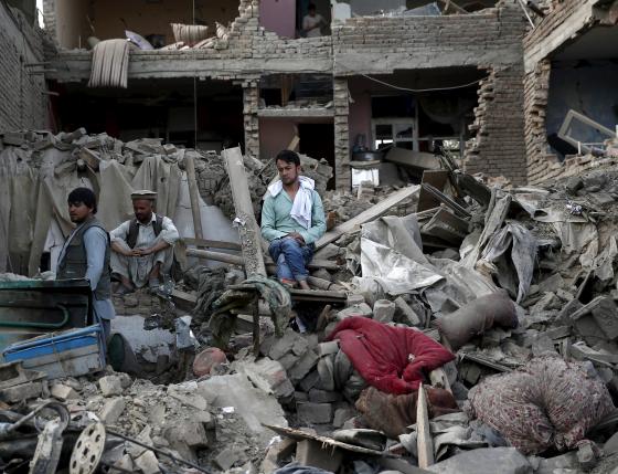 Men sit amid debris of their properties at the site a truck bomb blast in Kabul