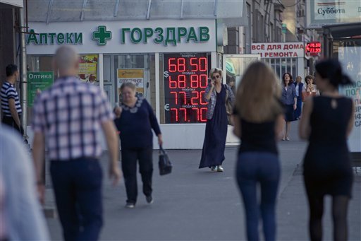 People walk past an exchange office sign showing the currency exchange rates in Moscow Russia Friday Aug. 21 2015. The Russian ruble currency is falling under the pressure of cheaper oil reviving concerns over the country's economic outlook. (AP Pho