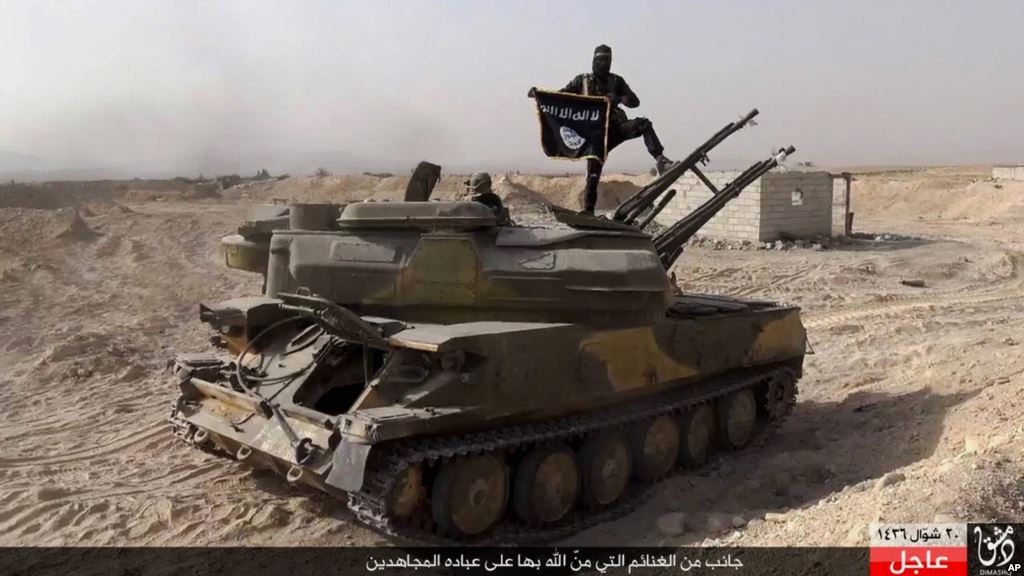 FILE- An Islamic State militant holds the group's flag as he stands on a tank captured from Syrian government forces in the town of al Qaryatayn southwest of Palmyra central Syria