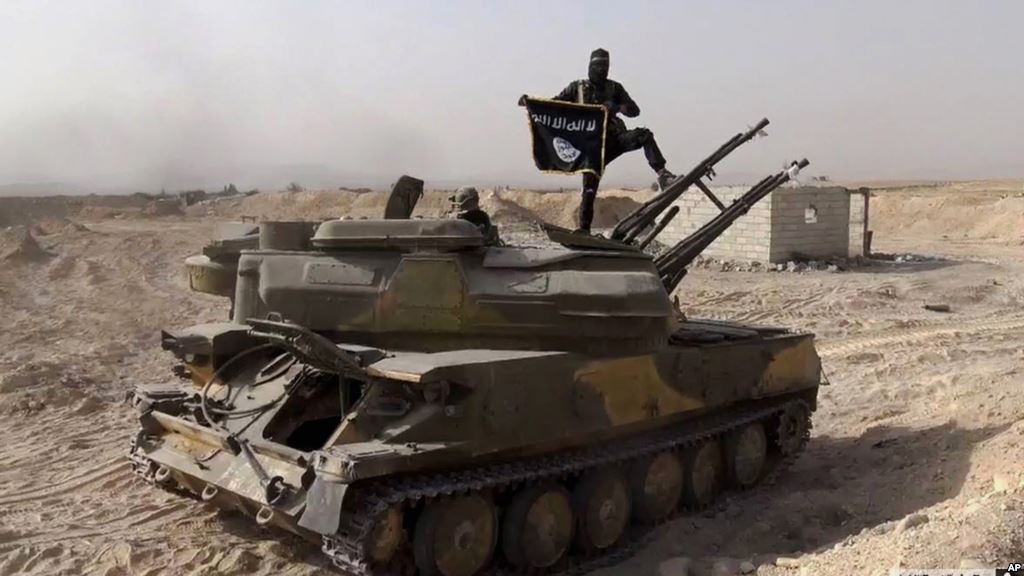 FILE- An Islamic State militant holds the group's flag as he stands on a tank captured from Syrian government forces in the town of al Qaryatayn southwest of Palmyra central Syria