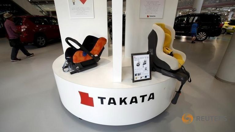 Visitors look at cars behind a logo of Takata Corp on its display at a showroom for vehicles in Tokyo Japan