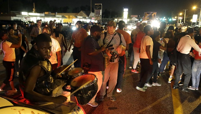 Protesters gather along West Florissant Avenue during a demonstration in Ferguson Mo. Tuesday Aug. 11 2015. The St. Louis suburb has seen demonstrations for days marking the anniversary of the death of 18-year-old Michael Brown whose shooting death