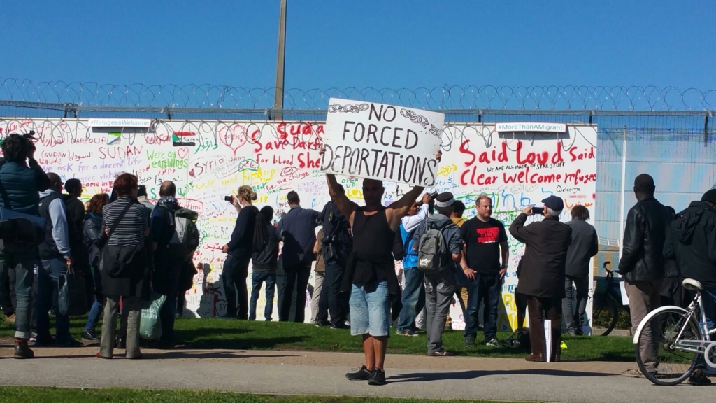 A migrant in Calais holds a'no forced deportations banner aloft