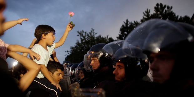 A small boy with a flower faces police attemping to keep refugees from crossing the border into Slovenia