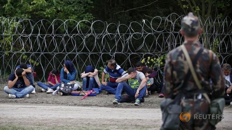 A soldier guards migrants detained after crossing the border from Serbia near Asttohatolom Hungary