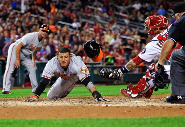 The Orioles’ Manny Machado sliding home to score past Nationals catcher Jose Lobaton in the fifth