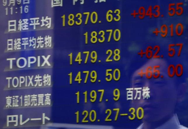 A pedestrian is reflected on a an electronic board showing the Japan's Nikkei average and other market indices including the exchange rate between the Japanese yen against the U.S. dollar at a brokerage in Tokyo Japan