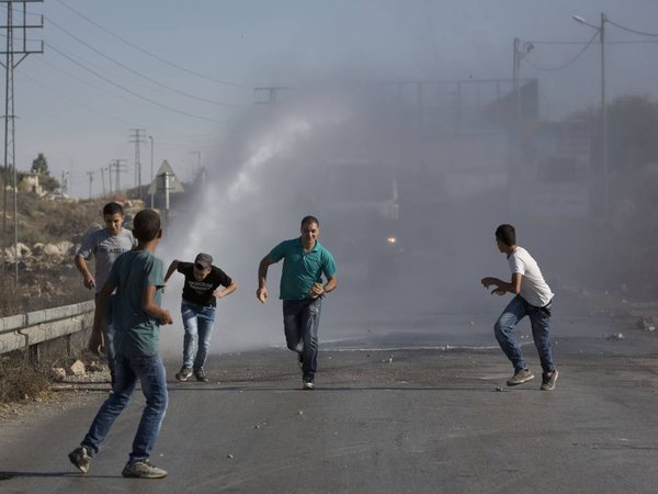 Palestinians run as Israeli troops use a water canon to disperse protesters during clashes in Jalazoun refugee camp near the West Bank city of Ramallah Friday Sept. 18 2015