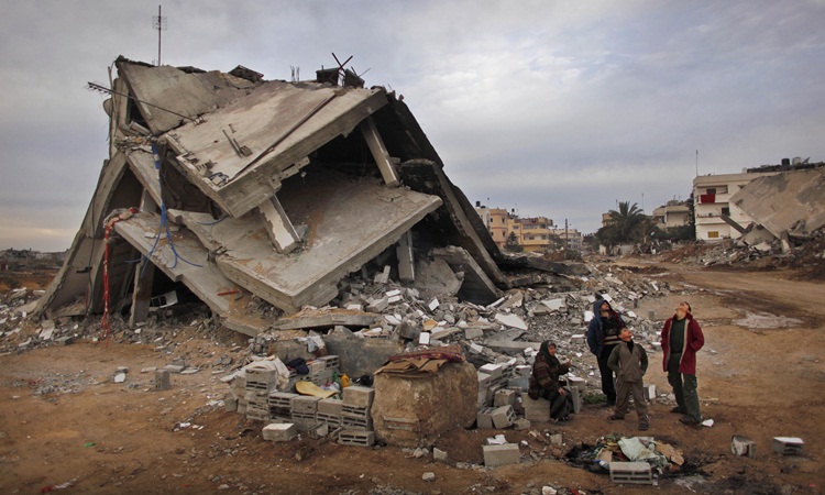 Palestinians look up at an Israeli air force unmanned drone as they stand in the rubble of their destroyed house in the area of east Jebaliya in the northern Gaza Strip that was devastated in the last Israeli military offensive Wednesday Jan. 28 2009