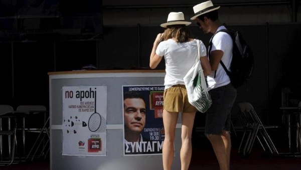 Tourists stand in front of an election kiosk of former Prime Minister Alexis Tsipras