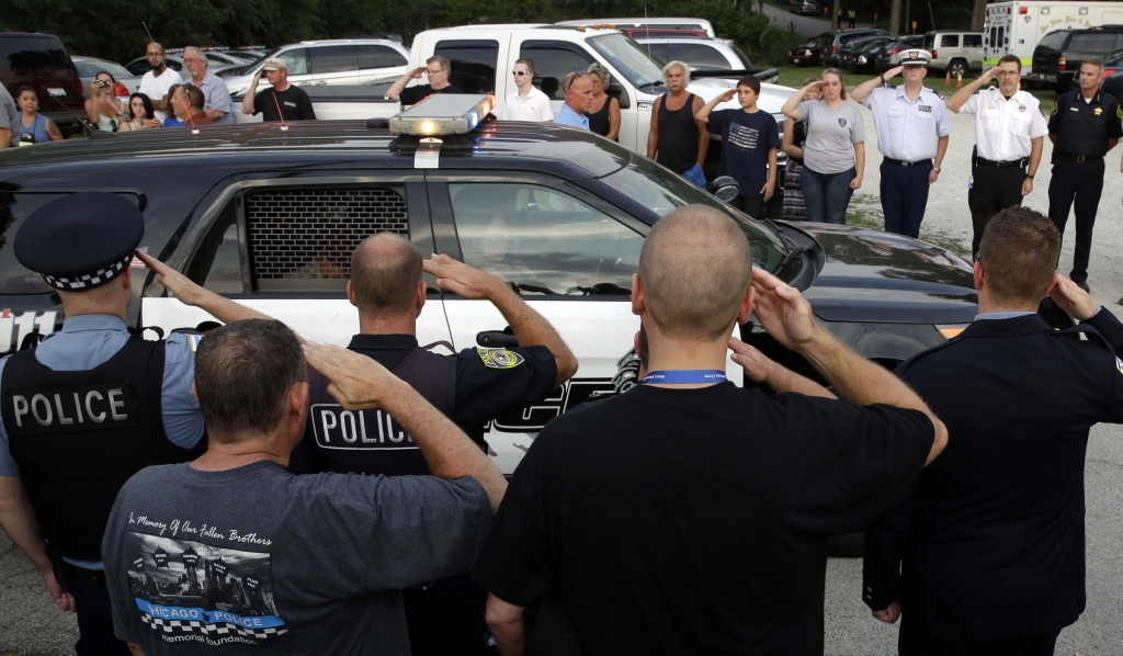 Officers salute as the family of slain Fox Lake police officer Lt. Joe Gliniewicz leave after a vigil at Lakefront Park to honor him Wednesday Sept. 2 2015 in Fox Lake Ill. Gliniewicz was shot and killed Tuesday while pursuing a group of suspicious