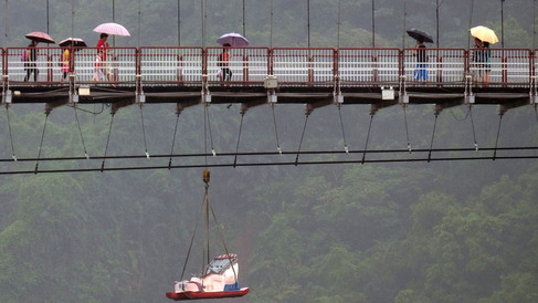 Local residents shelter themselves from the rain with umbrellas while crossing a suspension bridge in Pitan a popular area in Xindian district in New Taipei City