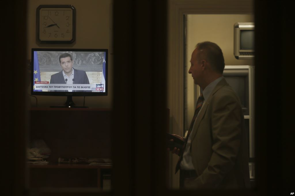 Greek Prime Minister Alexis Tsipras is seen on a screen during a televised address to the nation as a staffer of the Greek Presidential Palace looks on in Athens Aug. 20 2015