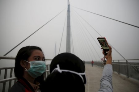 Girls take a selfie at the haze shrouded Batanghari River bridge in Jambi Indonesia Sumatra island