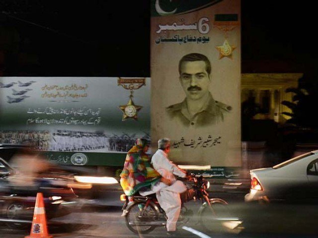 Traffic passing by a signboard honouring featuring Major Shabbir Sharif in Lahore