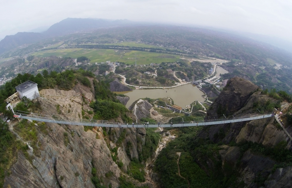 PINGJIANG CHINA- SEPTEMBER 24  Tourists walk on a suspension bridge made of glass at the Shiniuzhai National Geological Park