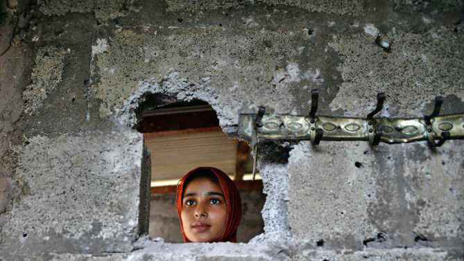 A Pakistani Kashmiri affected by cross border firing shows the damaged wall hit by mortar shell at her home