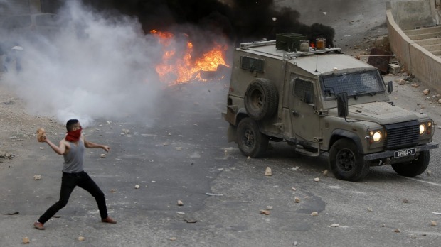 A Palestinian youth throws rocks at an Israeli military vehicle in the West Bank city of Nablus