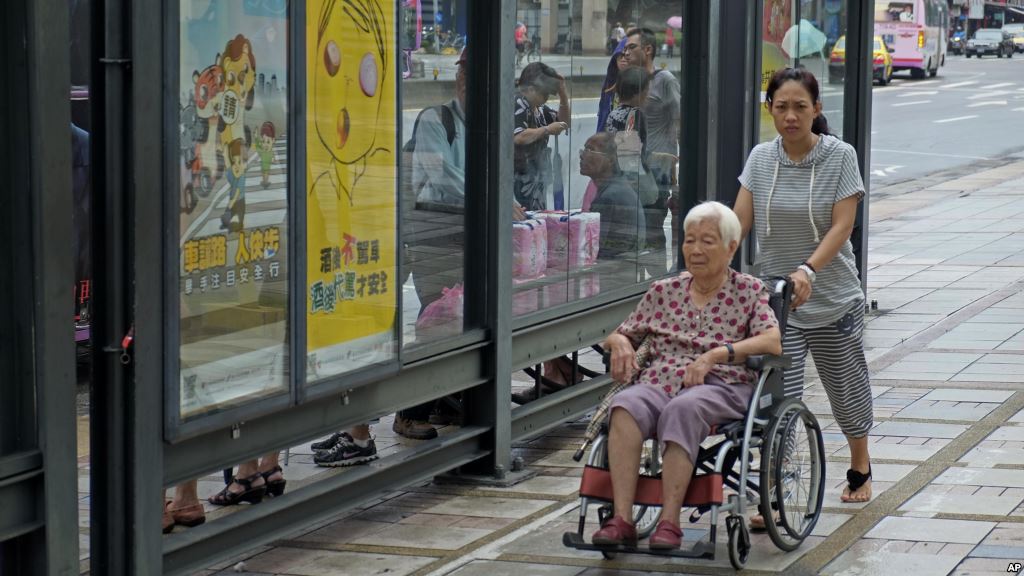 FILE- Caregiver pushes elderly wheelchair-bound woman through Taipei Taiwan Sept. 30 2013