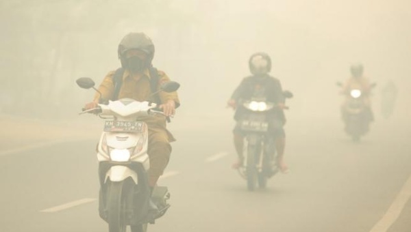 People ride motorcycles as haze shrouds the street in Palangkaraya Central Kalimantan province Indonesia